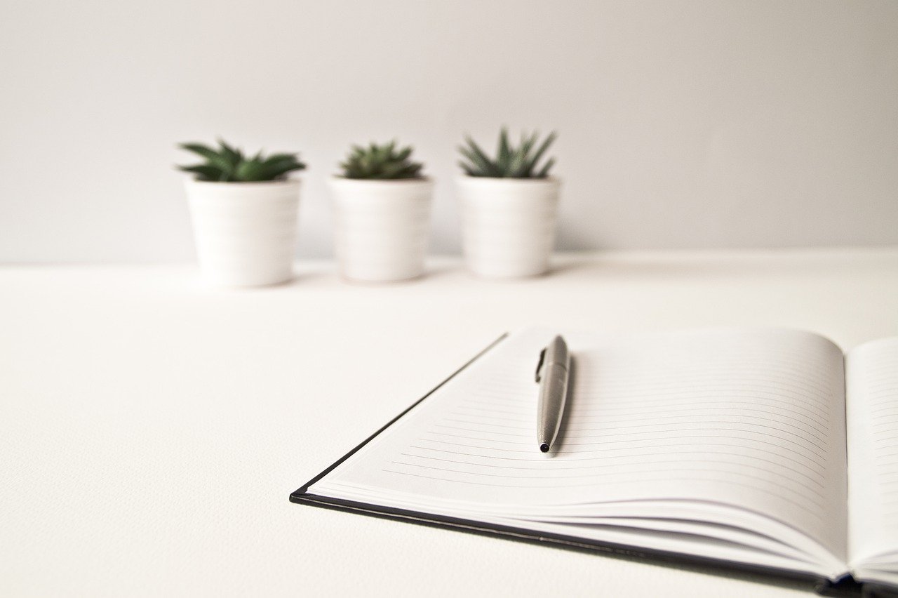 Notepad and pen sitting on a white table with three potted succulents